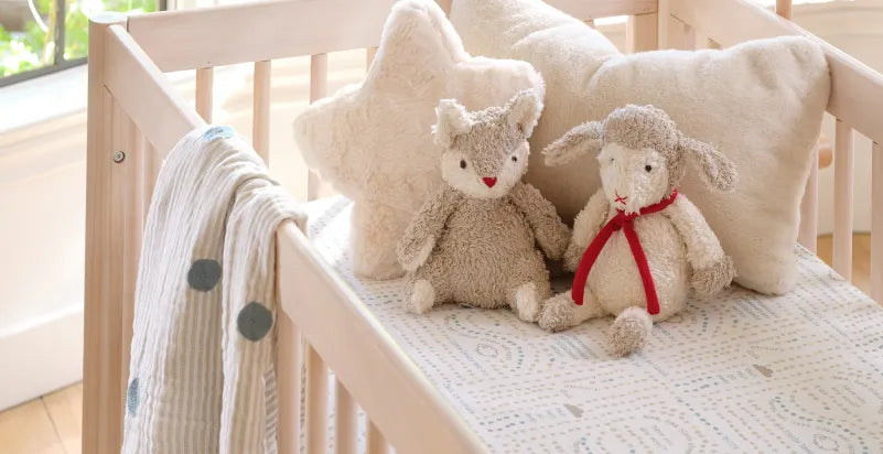 Organic stuffed animals and pillows in a wooden baby crib.