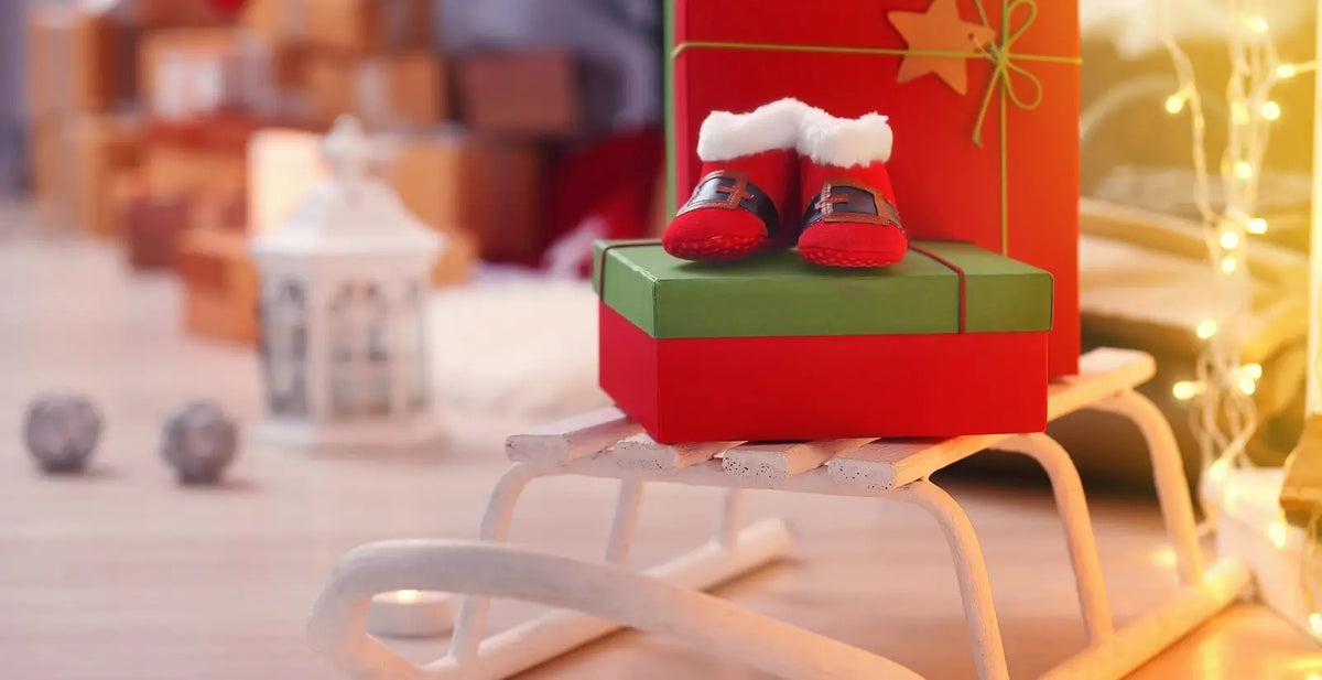 Baby booties and wrapped holiday gifts on a mini sleigh, representing newborn Christmas gift ideas