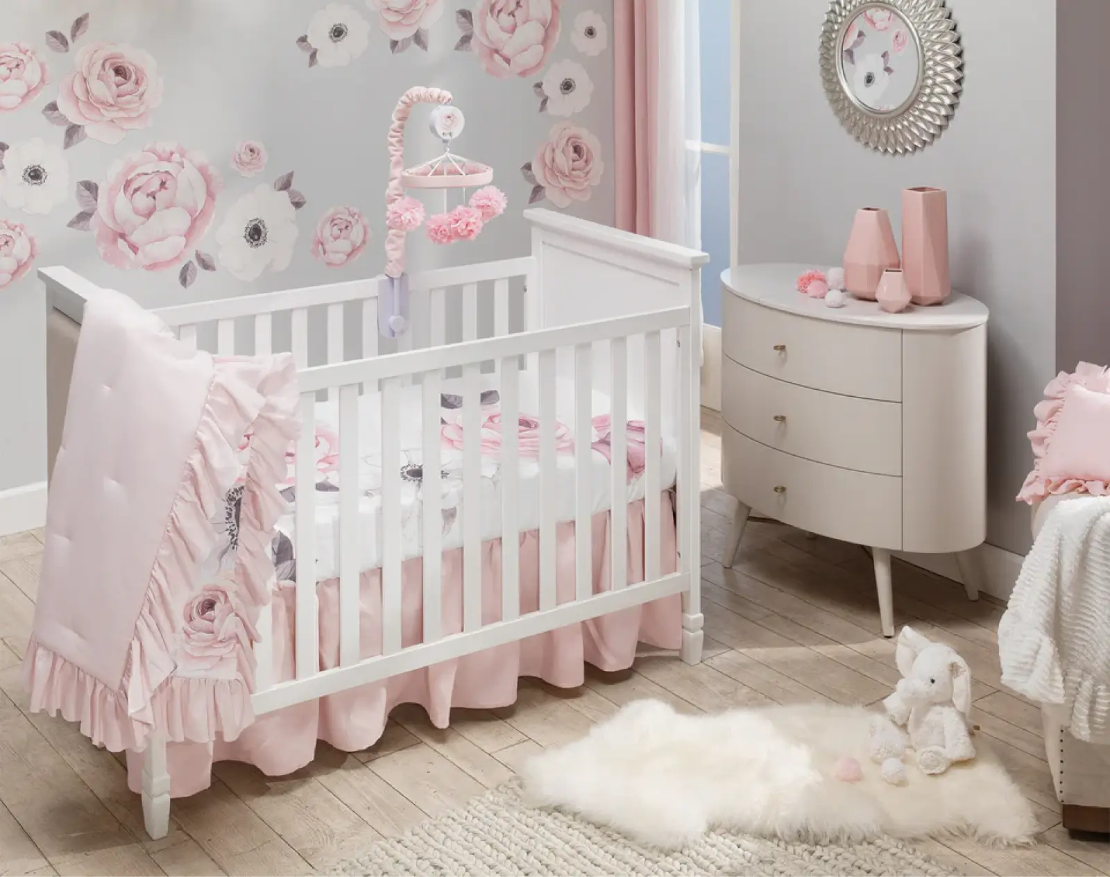 Elegant pink and gray floral baby nursery with rose wall decals, ruffled crib bedding, white furniture, and crystal chandelier.