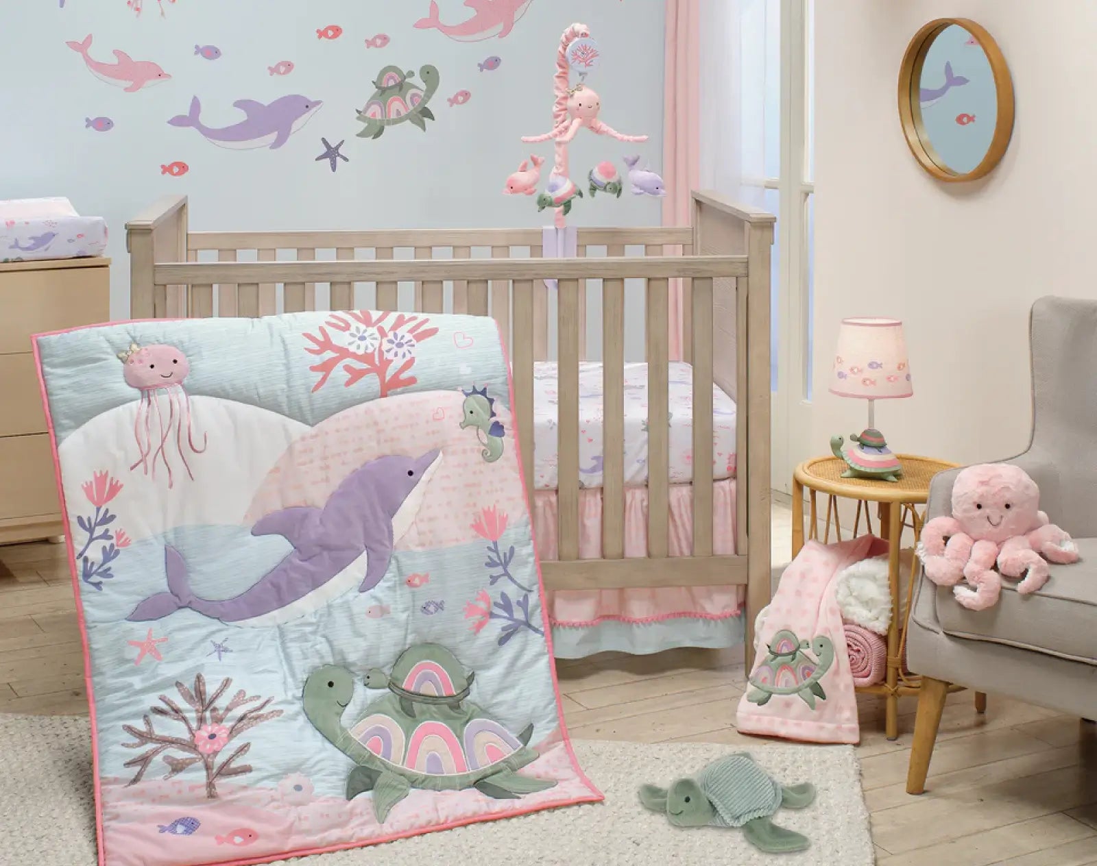 Ocean-themed baby girl nursery bedding set with whale, turtle, and jellyfish quilt in pastel pink and blue with matching wall decals.