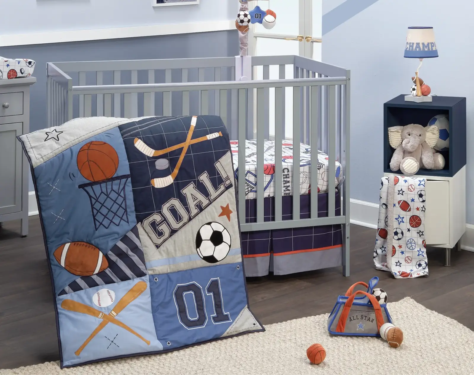 Sports-themed baby crib bedding set featuring football, soccer, basketball, and baseball designs with matching mobile and wall art.