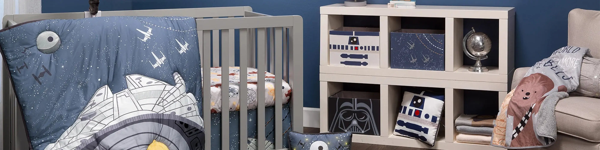 Star Wars baby crib bedding set with Millennium Falcon quilt, R2-D2 and Darth Vader storage bins, and Chewbacca pillow in a navy blue nursery.