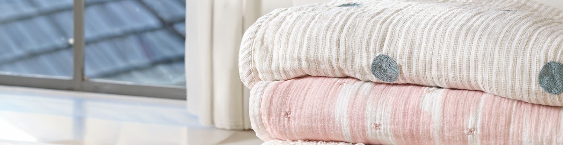 Stack of folded organic cotton baby blankets by a window.