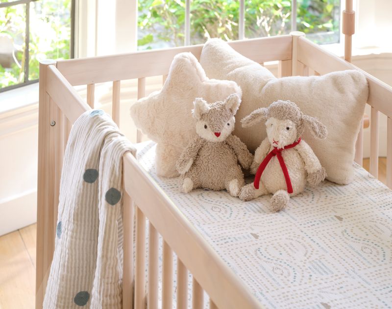 Organic baby crib bedding with plush toys and pillows.